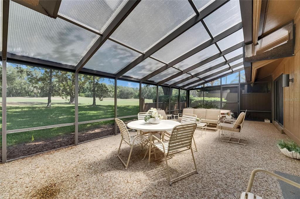 A screened-in patio with a sloped roof overlooks a grassy golf course — 29903 BAYWOOD LANE, WESLEY CHAPEL, FL