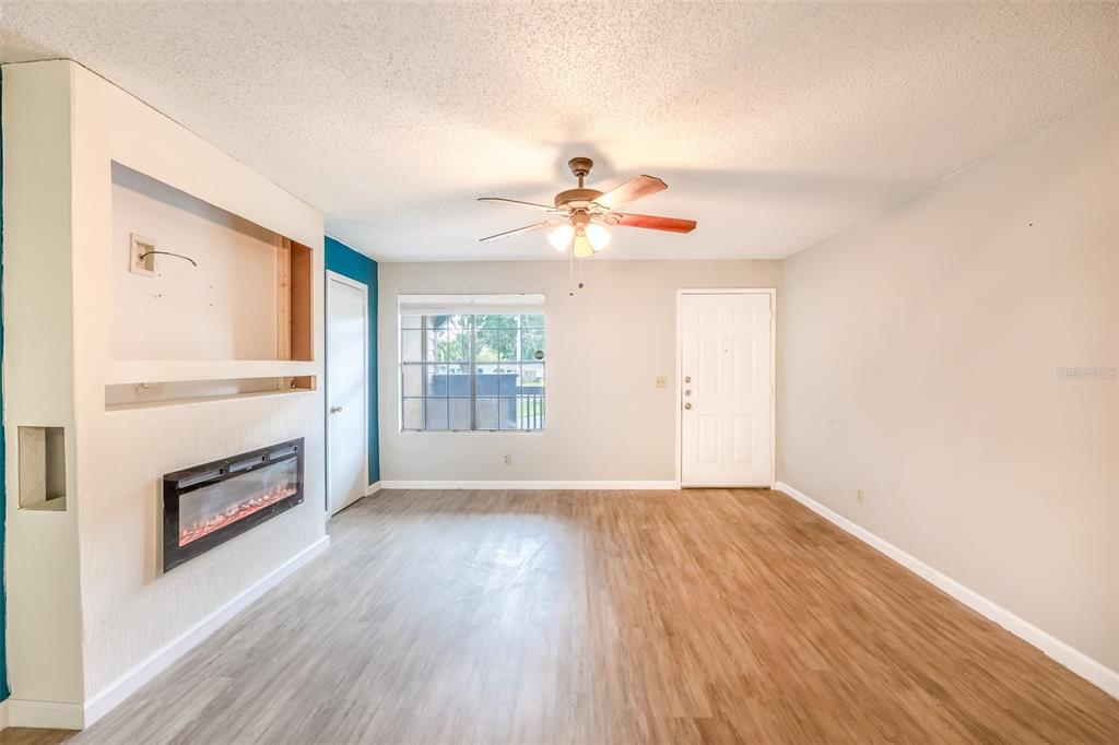 A living room features light wood-look flooring, a ceiling fan, and a wall-mounted electric fireplace — 360 LAKE ONTARIO COURT UNIT 202, ALTAMONTE SPRINGS, FL