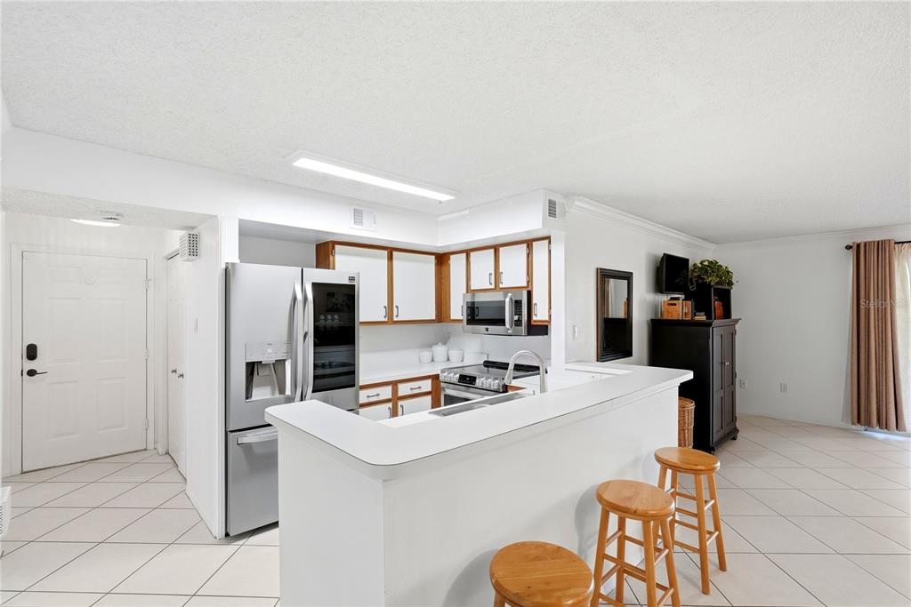 A kitchen with stainless steel appliances, white cabinets, and a breakfast bar overlooking the living area — 2400 FEATHER SOUND DRIVE UNIT 427, CLEARWATER, FL
