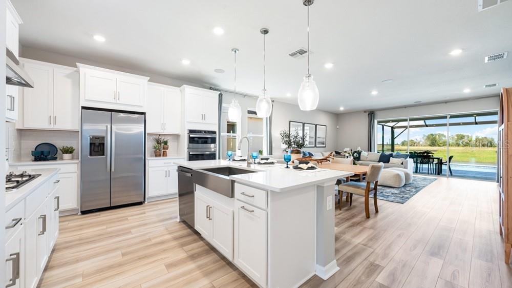 A modern kitchen with white cabinets, stainless steel appliances, and an island overlooks a living area — 12817 DOCKYARD TRAIL, PALMETTO, FL