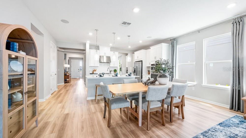 A bright, open-concept kitchen and dining area featuring light wood floors and white cabinetry — 12817 DOCKYARD TRAIL, PALMETTO, FL