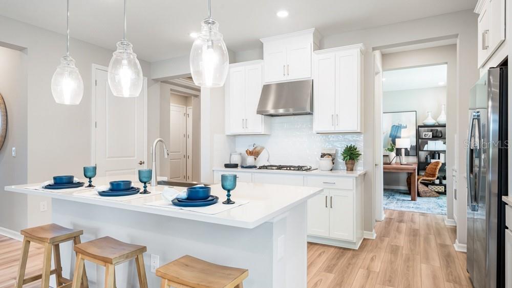 A modern kitchen features white cabinets, a quartz island with bar stools, and stainless appliances — 12817 DOCKYARD TRAIL, PALMETTO, FL