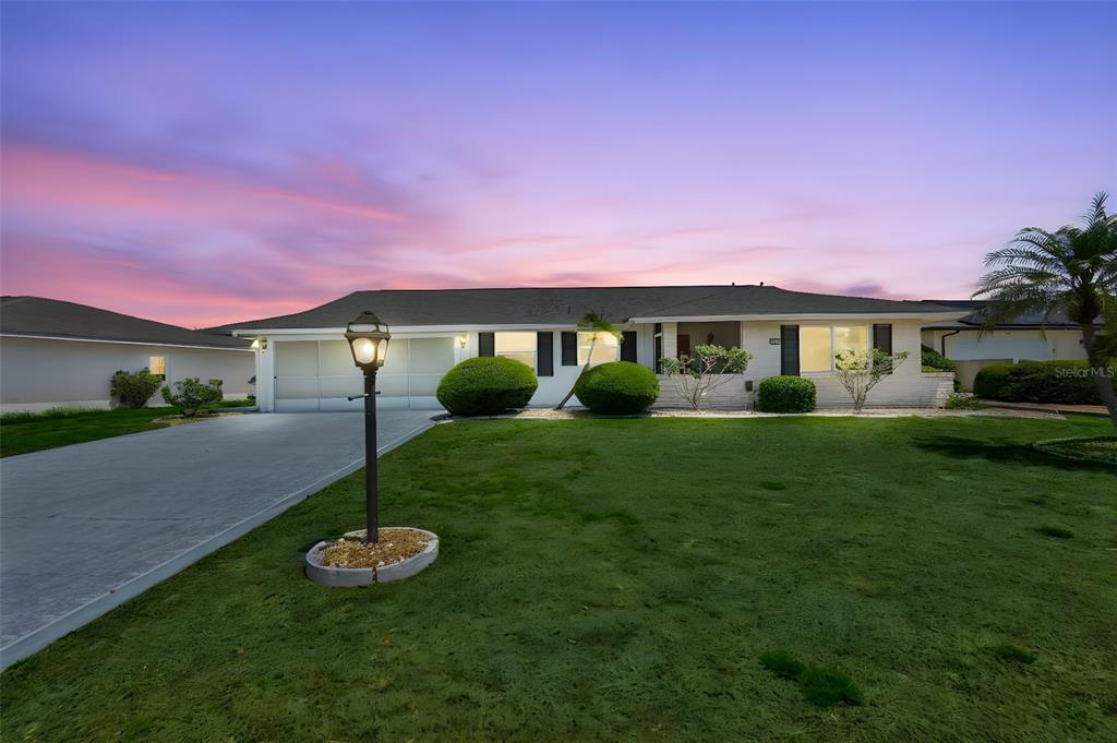 A single-story house with a white exterior, a concrete driveway, and a manicured front lawn — 1525 ALLEGHENY DRIVE, SUN CITY CENTER, FL