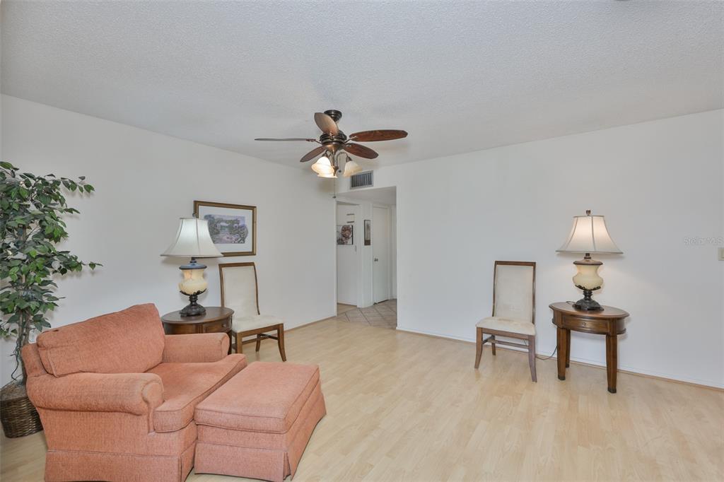 A living room features light wood flooring, an orange armchair with ottoman, and two lamps — 1525 ALLEGHENY DRIVE, SUN CITY CENTER, FL