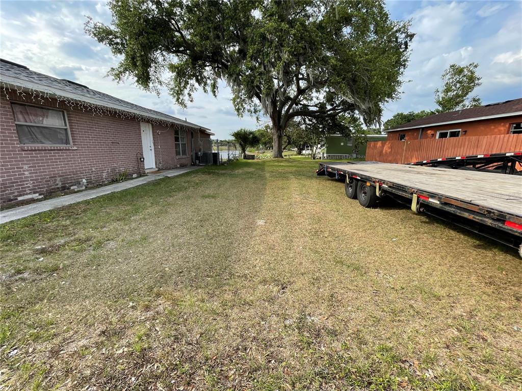 A grassy yard sits between a brick house and a flatbed trailer under a tree — SKYVIEW DRIVE, LAKELAND, FL