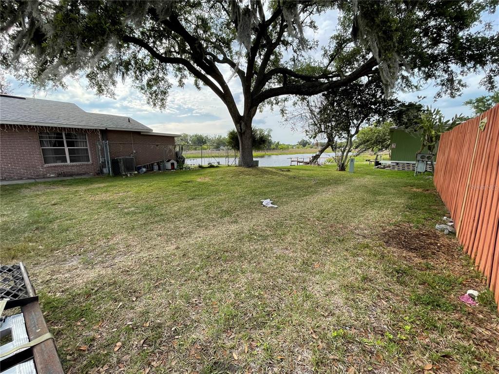 A grassy backyard features a large oak tree, a brick house, and a wooden fence — SKYVIEW DRIVE, LAKELAND, FL