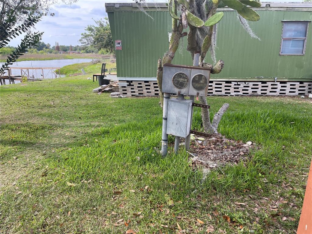 An outdoor electrical meter and service panel stand in the grass beside a green mobile home — SKYVIEW DRIVE, LAKELAND, FL