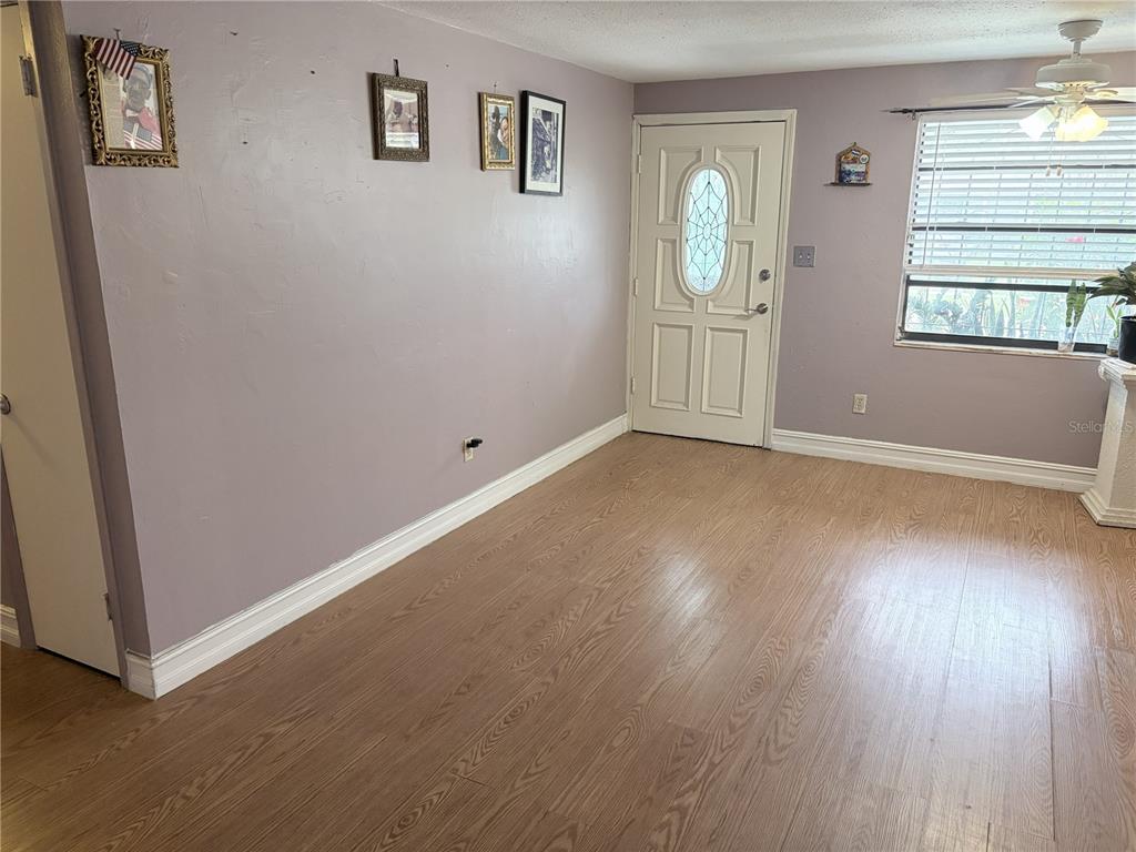 An empty room features light wood-look flooring, lavender walls, a white front door, and blinds — 4802 E CURTIS STREET, TAMPA, FL