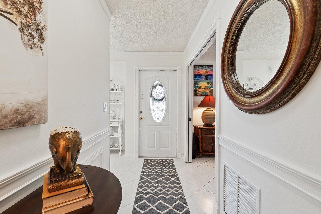 A white entryway features a patterned runner, a round mirror, and an elephant statue — 5010 Privet Place # 101, Delray Beach FL 33484, DELRAY BEACH, FL