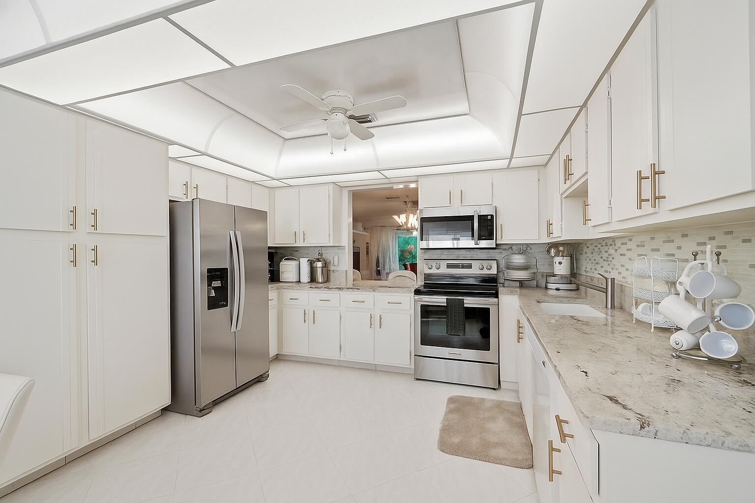 A bright kitchen features white cabinets, stainless steel appliances, and light-colored granite countertops — 5010 Privet Place # 101, Delray Beach FL 33484, DELRAY BEACH, FL