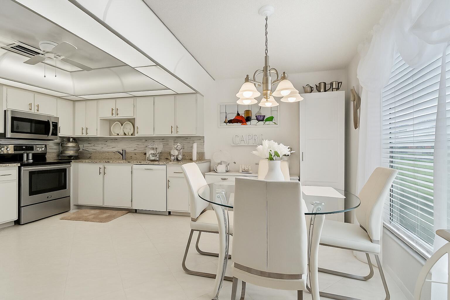 A bright kitchen features white cabinetry, stainless steel appliances, and a glass-topped dining table — 5010 Privet Place # 101, Delray Beach FL 33484, DELRAY BEACH, FL