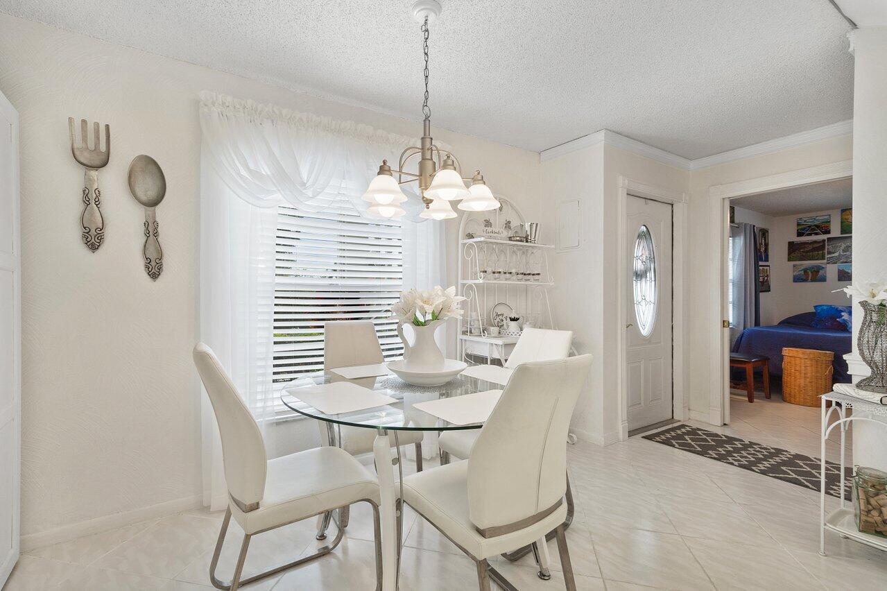 A bright dining room features a glass table, four white chairs, and a chandelier — 5010 Privet Place # 101, Delray Beach FL 33484, DELRAY BEACH, FL