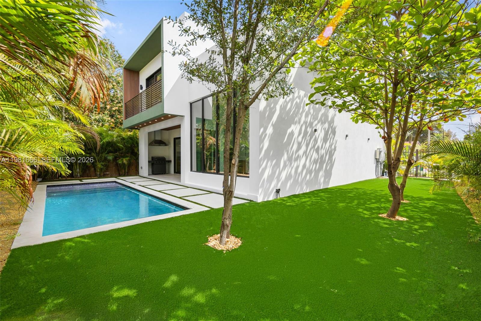 A modern white two-story house features a swimming pool and a green lawn with trees — 569 NW 44th St, Miami FL 33127, MIAMI, FL