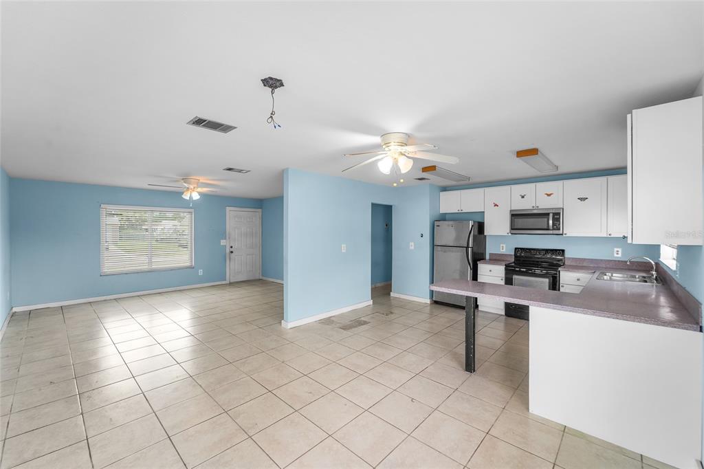 An open-concept kitchen and living area with light blue walls and beige tile flooring — 4577 MARALDO AVENUE, NORTH PORT, FL