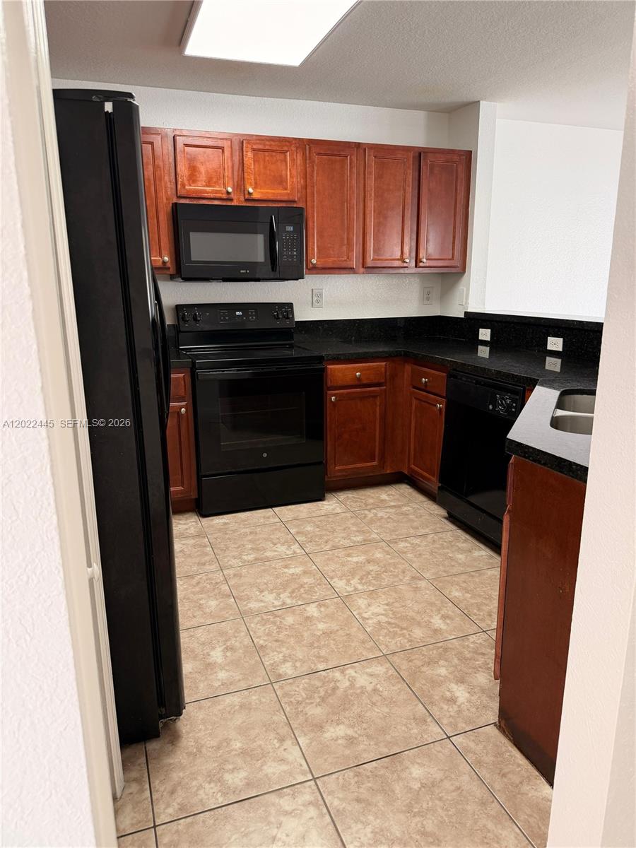 A kitchen features dark wood cabinets, black appliances, and dark countertops over tiled flooring — 3172 SW 128th Ter # 148, Miramar FL 33027, MIRAMAR, FL