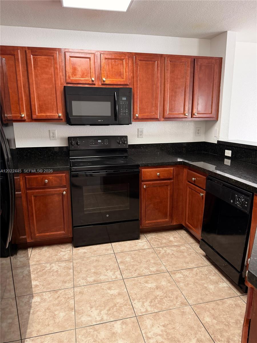 A kitchen features cherry wood cabinets, black appliances, and dark granite countertops over tiled floors — 3172 SW 128th Ter # 148, Miramar FL 33027, MIRAMAR, FL