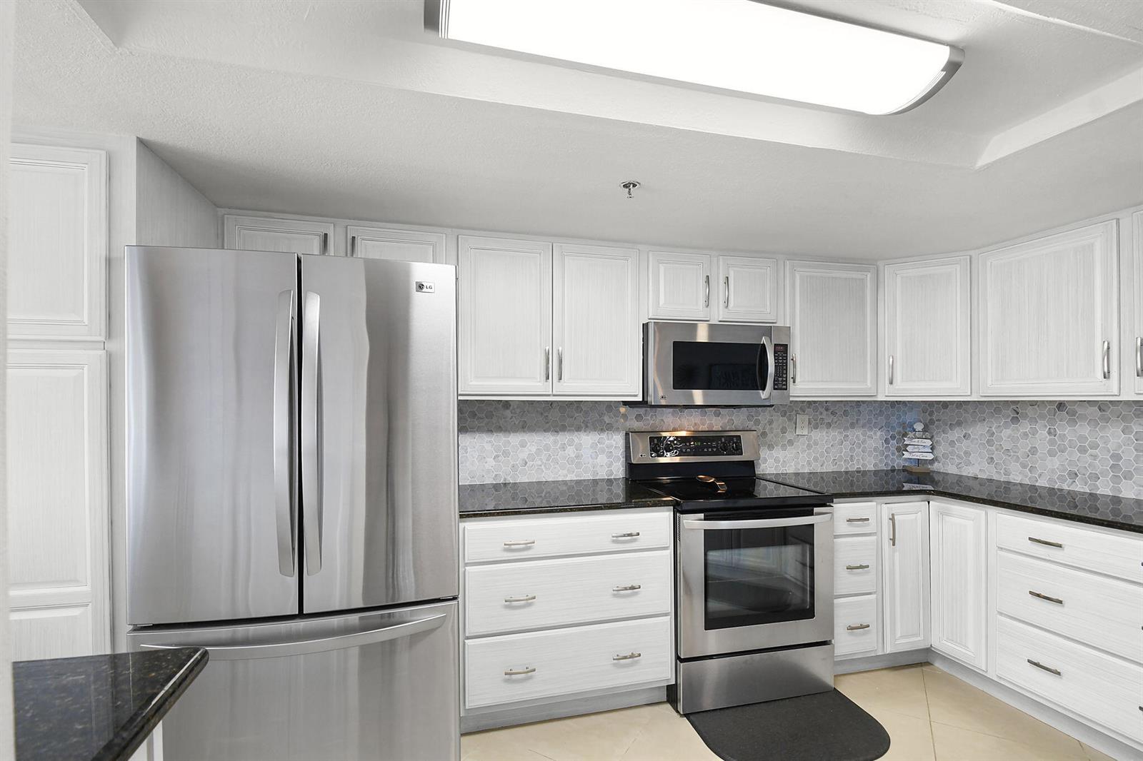 A kitchen with white cabinets, stainless steel appliances, black countertops, and a hexagonal tile backsplash — 3870 N Highway A1a # 805, Fort Pierce FL 34949, FORT PIERCE, FL