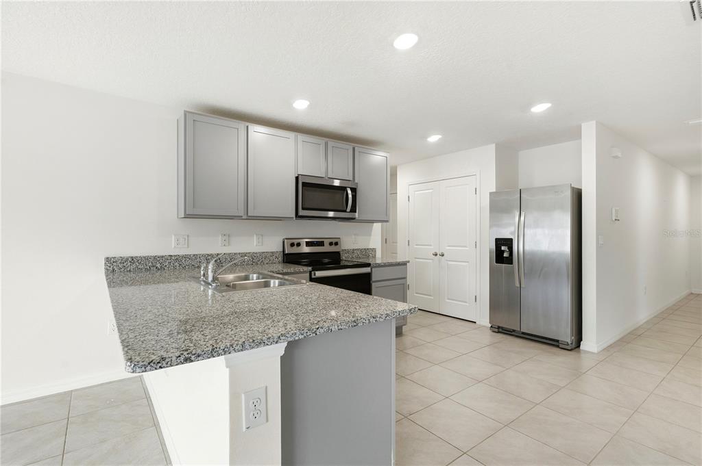 A kitchen features gray cabinets, granite countertops, stainless steel appliances, and light tile flooring — 13322 GOLDEN LIME AVENUE, SPRING HILL, FL