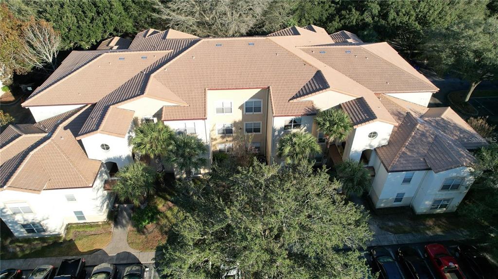 An aerial view of a multi-story apartment building with a tiled roof and surrounding trees — 826 CAMARGO WAY UNIT 303, ALTAMONTE SPRINGS, FL