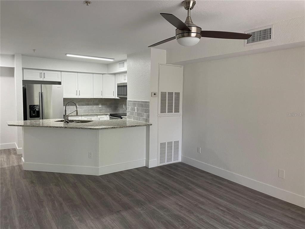 A kitchen with white cabinets and a granite breakfast bar opens to a living area — 826 CAMARGO WAY UNIT 303, ALTAMONTE SPRINGS, FL