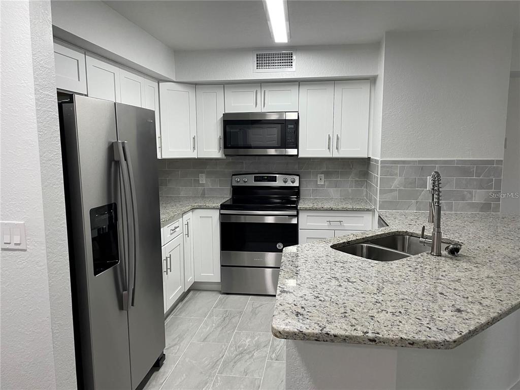 A kitchen features white cabinets, stainless steel appliances, granite countertops, and a gray tile backsplash — 826 CAMARGO WAY UNIT 303, ALTAMONTE SPRINGS, FL