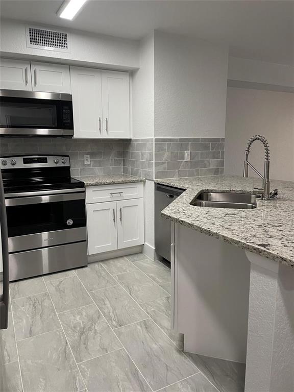 A kitchen features white cabinets, stainless steel appliances, granite countertops, and gray tile flooring — 826 CAMARGO WAY UNIT 303, ALTAMONTE SPRINGS, FL