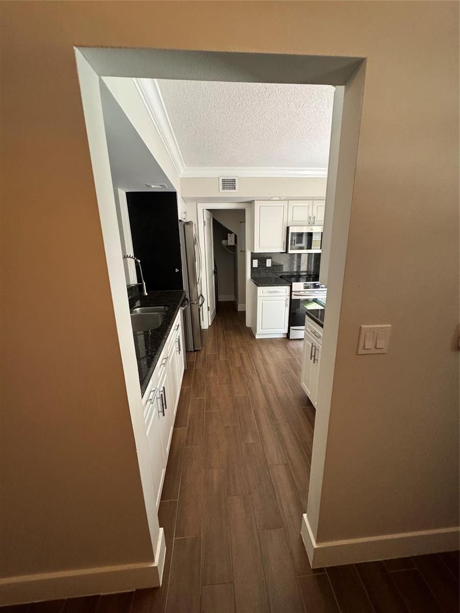 A view through a doorway into a kitchen with white cabinets and wood-look flooring — 7741 La Mirada Drive, Boca Raton FL 33433, BOCA RATON, FL