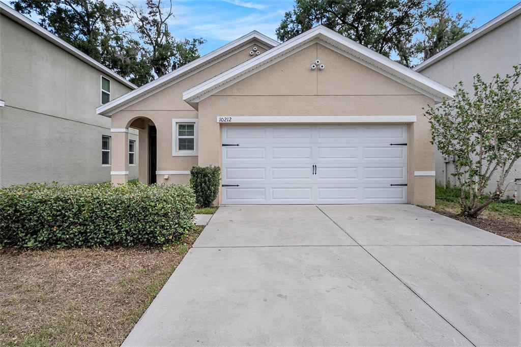 A single-story house features a beige stucco exterior, a white garage door, and a driveway — 10212 HAWK STORM AVENUE, TAMPA, FL