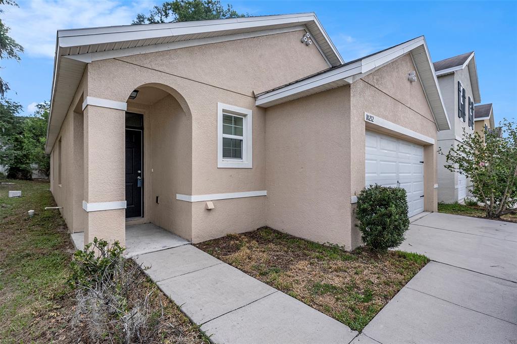 A tan stucco single-story house features a front-facing garage and a covered entryway — 10212 HAWK STORM AVENUE, TAMPA, FL