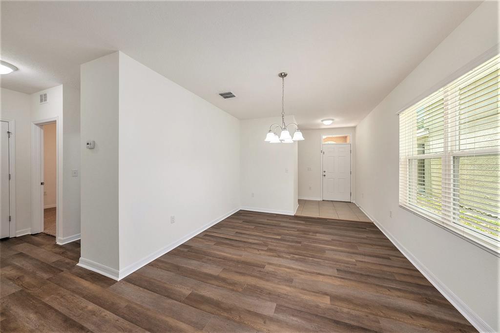 An empty dining area features wood-look flooring, a white chandelier, and a large window — 10212 HAWK STORM AVENUE, TAMPA, FL