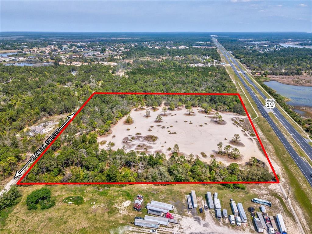 An aerial view shows a rectangular, sandy vacant lot bordered by trees and a highway — 15.7 Acres COMMERCIAL WAY, WEEKI WACHEE, FL