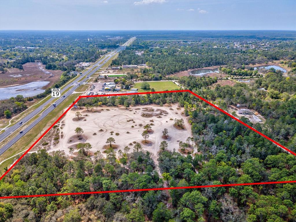 An aerial view shows a large, cleared sandy lot outlined in red next to a highway — 15.7 Acres COMMERCIAL WAY, WEEKI WACHEE, FL