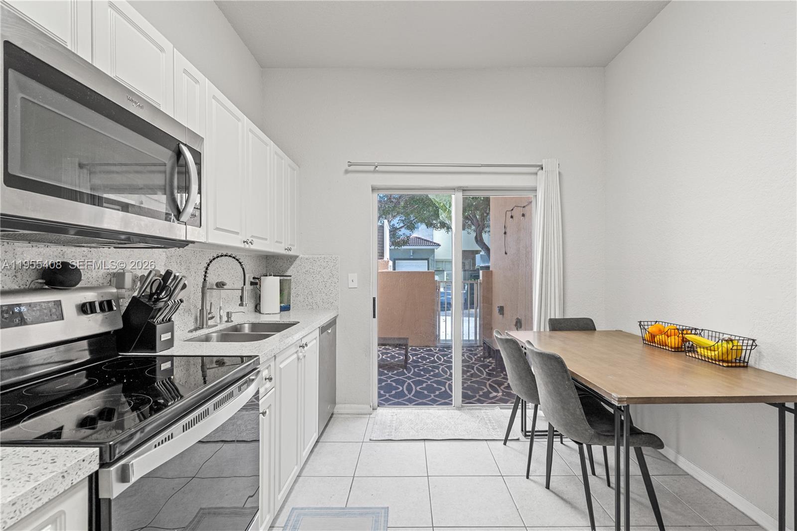 A kitchen with white cabinets, stainless steel appliances, and a dining area beside a patio — 1940 SE 24th Ter, Homestead FL 33035, HOMESTEAD, FL