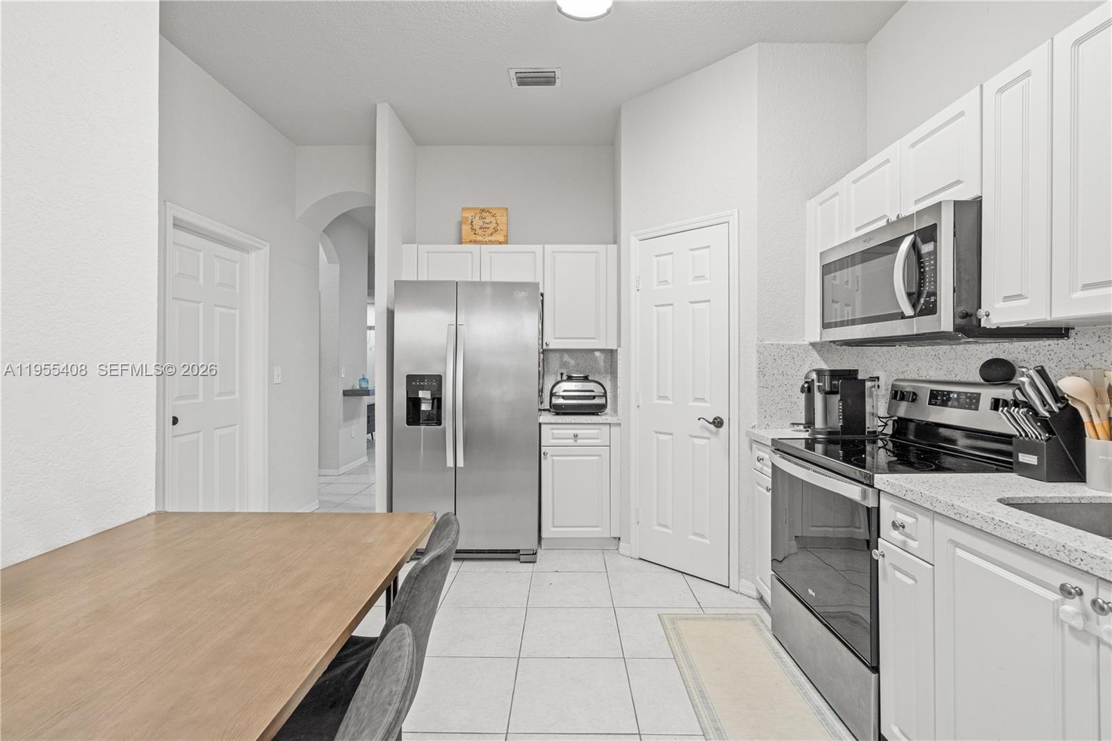 A kitchen features white cabinets, stainless steel appliances, and a light-colored tiled floor — 1940 SE 24th Ter, Homestead FL 33035, HOMESTEAD, FL