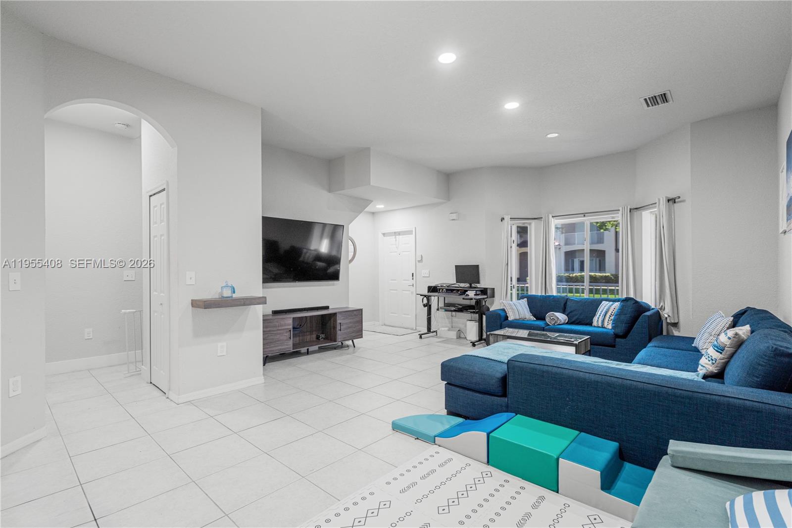 A living room features light tile floors, a blue sectional sofa, and a wall-mounted television — 1940 SE 24th Ter, Homestead FL 33035, HOMESTEAD, FL