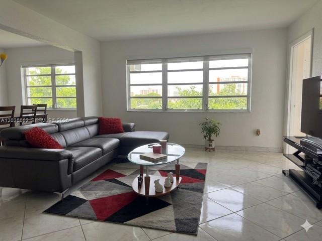 A living room features a grey sectional sofa, a glass coffee table, and tile flooring — 1530 NE 191st St # 305, Miami FL 33179, MIAMI, FL