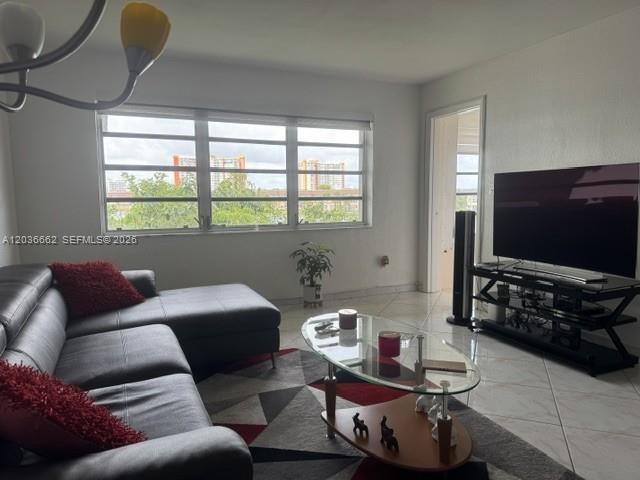 A living room features a dark leather sectional, a glass coffee table, and a television — 1530 NE 191st St # 305, Miami FL 33179, MIAMI, FL