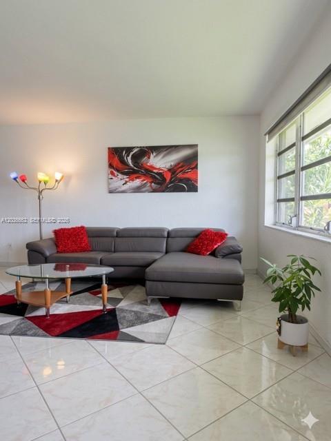 A living room features a gray sectional sofa, a glass coffee table, and tiled floors — 1530 NE 191st St # 305, Miami FL 33179, MIAMI, FL