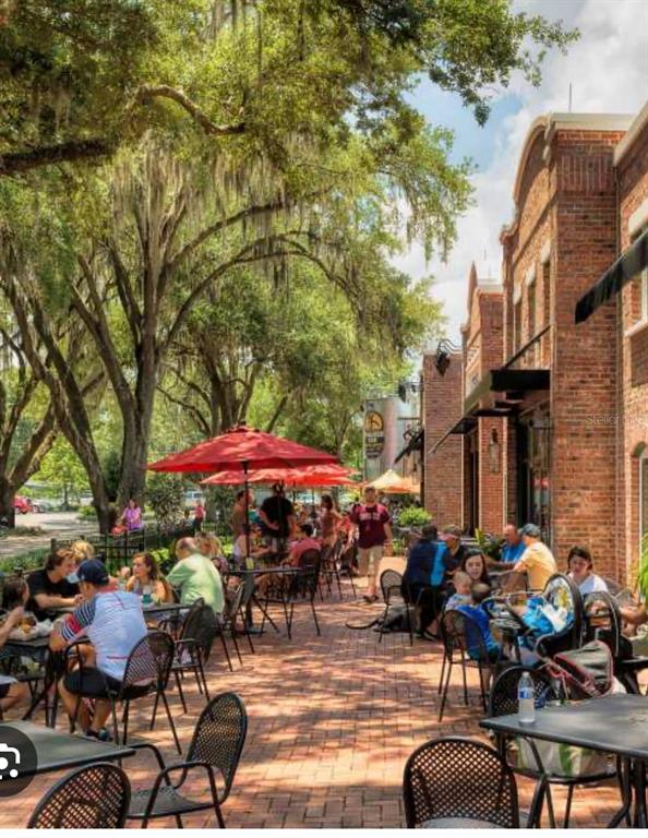 Outdoor brick patio with dining tables and red umbrellas under large oak trees — 47 OAK STREET, WINTER GARDEN, FL