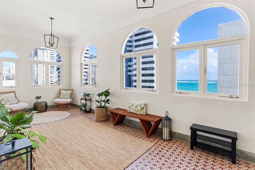 A sunroom features arched windows, patterned tile flooring, and views of the ocean and buildings — 1506 ASHFORD UNIT PH, SAN JUAN, PR