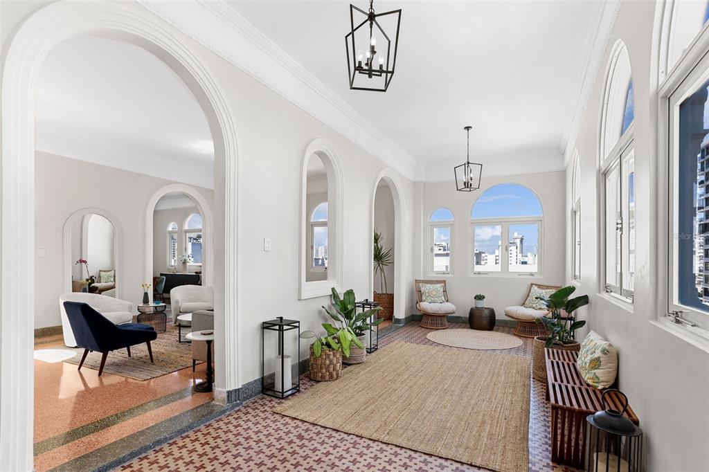 A sunroom with arched doorways, patterned tile floors, and large windows overlooking a city skyline — 1506 ASHFORD UNIT PH, SAN JUAN, PR