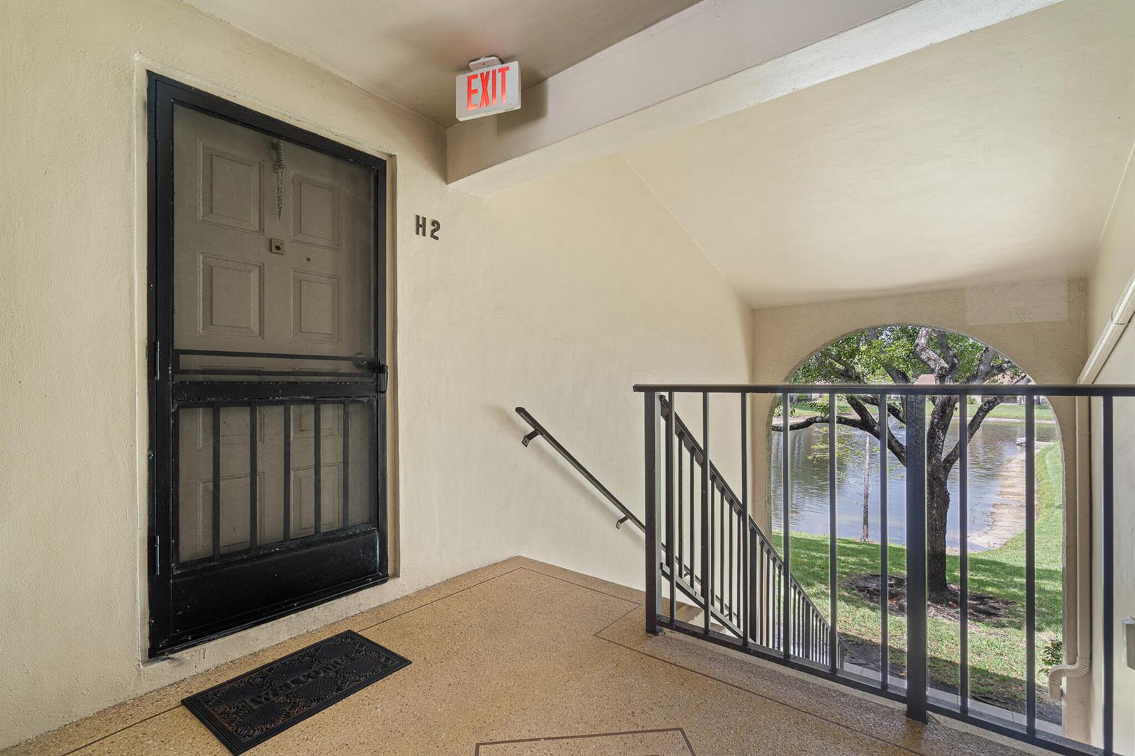 An apartment entryway with a black screen door, a welcome mat, and a stairwell railing — 610 Sea Pine Way # H2, FL 33415, FL