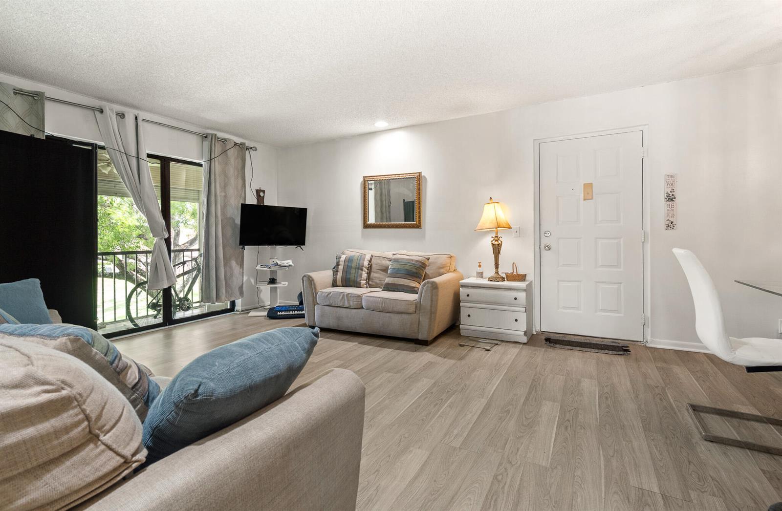 A living room features light wood-look flooring, a beige sofa, a mirror, and a balcony — 610 Sea Pine Way # H2, FL 33415, FL