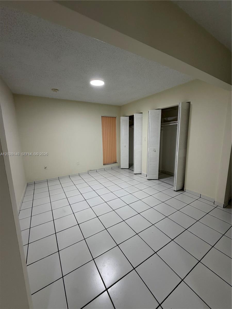 An empty room features white tiled floors, light-colored walls, and two open louvered closets — MIAMI, FL