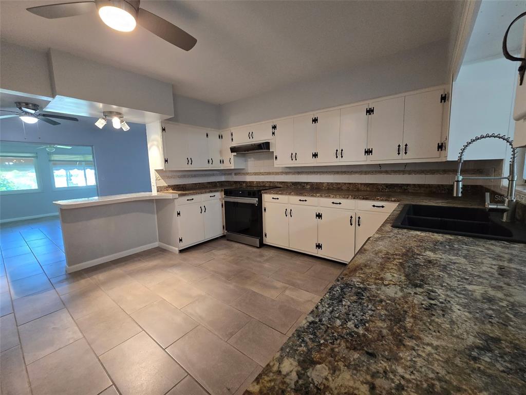 A kitchen features white cabinets, granite countertops, a black sink, and light-colored tile flooring — 507 LAKE LULU DRIVE, WINTER HAVEN, FL
