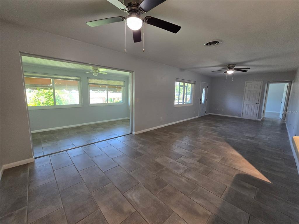 A living room with gray tile flooring, two ceiling fans, and a large sliding door — 507 LAKE LULU DRIVE, WINTER HAVEN, FL