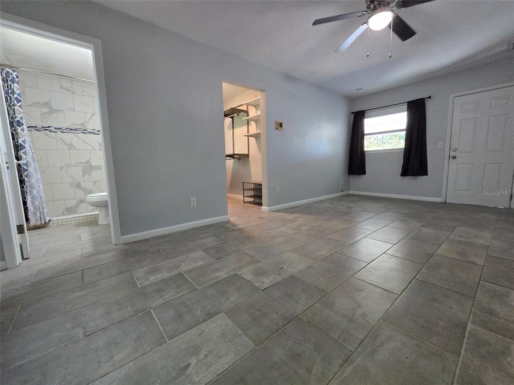 A bedroom with gray tile flooring, a ceiling fan, a walk-in closet, and an ensuite bathroom — 507 LAKE LULU DRIVE, WINTER HAVEN, FL