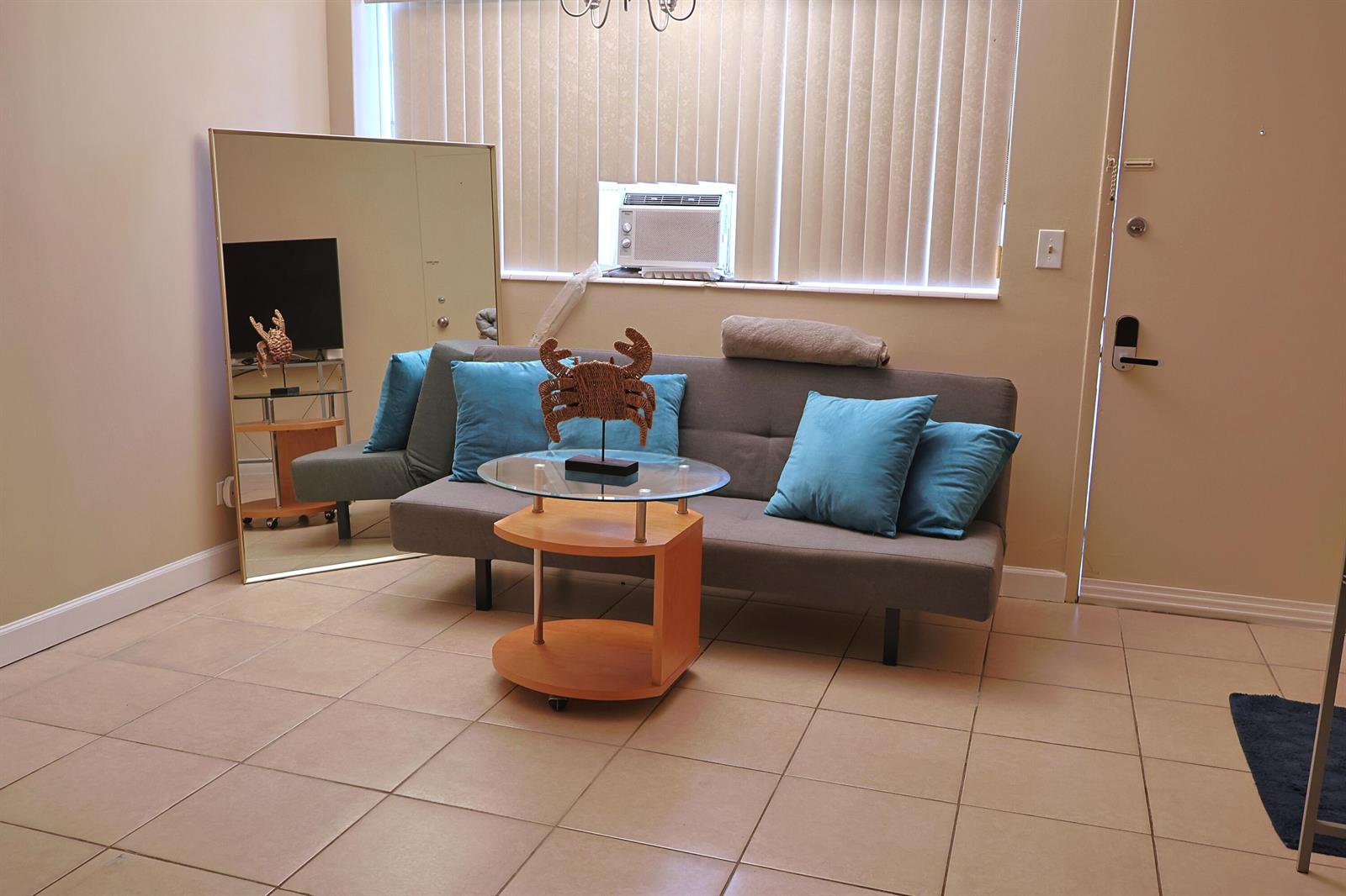 A living room features a gray sofa, a glass-topped side table, and a large floor mirror — 26 Diplomat Parkway # 2280, FL 33009, FL