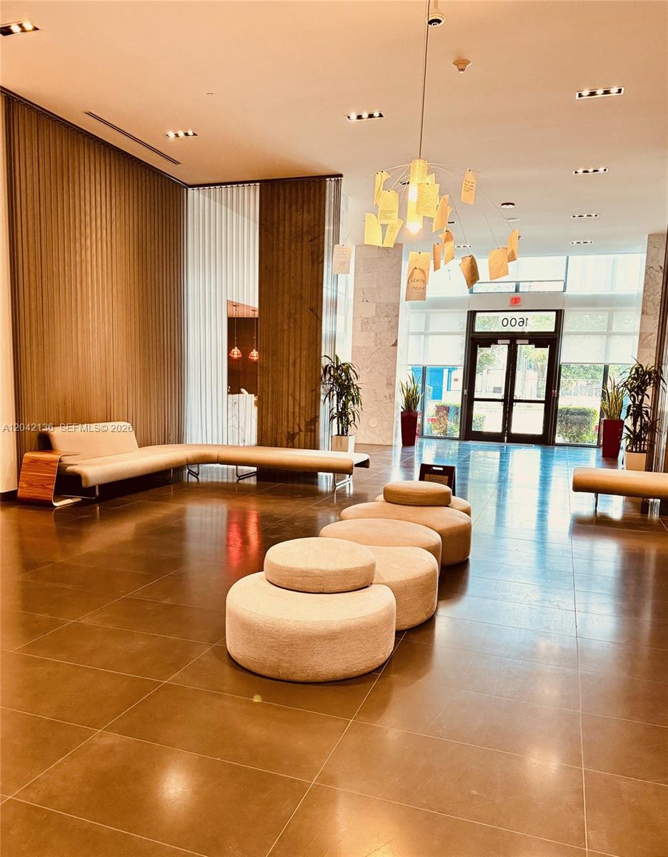 A modern lobby features a long beige sofa, circular ottomans, and a hanging paper art installation — 1600 NE 1 # 1915, Miami FL 33132, MIAMI, FL