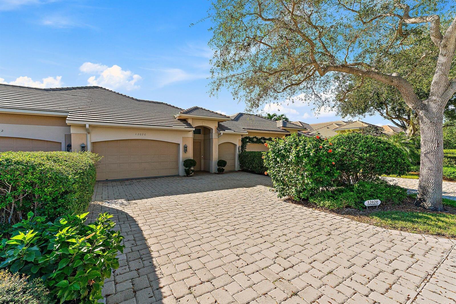 A beige house with a tiled roof and a paved driveway sits under a large tree — 12020 SE Birkdale Run, Jupiter FL 33469, JUPITER, FL